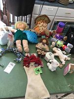 Photo showing assorted stuffed toys, dolls, puppet, and small decorative items spread on a green table.