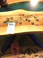 Top down image of various tie clips and cuff links arranged on a wooden table, all items clearly visible, including some with decorative patterns and different metal finishes.