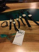 Seven Timex wristwatches laid out on a wooden surface including various leather and metal bands, with a tag marked '802 Watches'