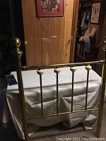 Full view of twin brass headboard lying flat on a table against a wood paneled wall.