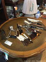 Overall assortment of kitchen utensils including knives, spreaders, forks, juicer, and spatulas on round wooden table.