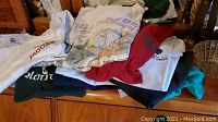 Stack of shirts and sweatshirts including white Jaguar t-shirt, Stone Mountain graphic tee, red shirt, dark green shirt and others