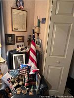 Armchair with multiple items displayed: brass eagle sculptures, Lincoln bust, flag, stacked framed prints.