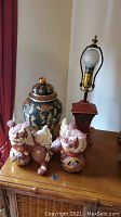 Photo showing two porcelain Chinese-style dragons, chinoiserie ginger jar, and Asian style lamp on wooden surface.