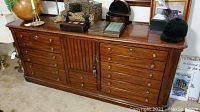 Solid wood dresser with multiple drawers and central cabinet in warm brown finish, brass knobs visible on drawers.