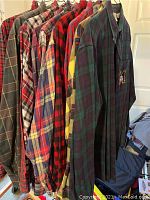 Photo of multiple long sleeve flannel shirts in assorted plaids and colors hanging on a clothing rack.