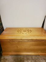 Front view of the blonde wood hope chest showing the whole chest with carved center design on lid.
