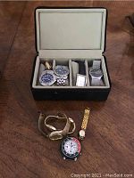 Watches displayed in an open black leather case and arranged outside of case on wooden surface