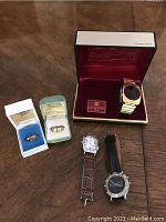 All five items displayed on wooden surface: two ring boxes, three watches.