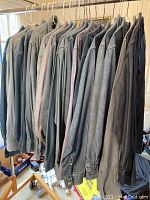 Photo of 20 men's long sleeve denim and button front shirts hanging on a rack showing various shades of denim and one non-denim shirt