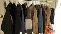 Photo showing several men's jackets and slacks hanging on a clothing rack, displaying a mix of colors and styles including outerwear and casual pants.