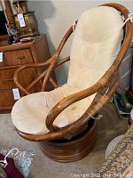 Rattan swivel Papa San chair with beige cushion showing curved rattan frame and padded seat.
