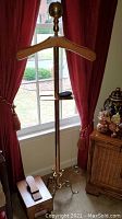 Full view of 55" tall brass and wood jacket valet with shoe valet and curtains in the background