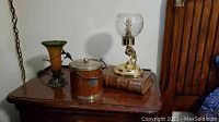 Photo showing the brass hummingbird lamp, wooden ice bucket, decorative book box, and brass fish candle holder on a wooden surface.