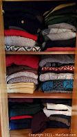 Folded vintage Bill Cosby sweaters on three wooden shelves, showing various colors and knit styles