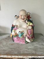 Front view of entire statue showing Laughing Buddha seated with children and prayer beads.