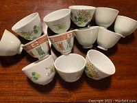Top view of 12 small hand-painted Chinese porcelain teacups on wooden surface showing floral and traditional designs.