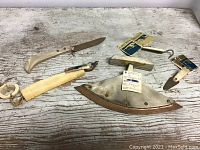 Photo showing entire group of six Inuit Indigenous tools on a wooden surface. Items include knives, hooks, and cutting tools primarily made of ivory and metal with original labels attached to some.