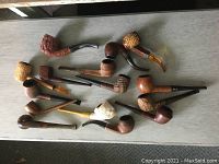 Overview of 13 assorted antique tobacco pipes of various woods and styles laid on flat surface