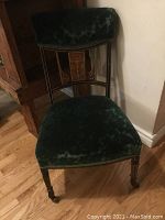 Full view of antique chair showing green velvet upholstered seat and backrest above inlaid wood detail on backrest and wooden legs with small casters.