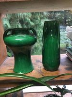 Photo of two antique green glazed ceramic vases on wooden shelf, one tall and narrow, one shorter and wider with handles.