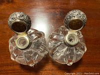 Top view of two squat crystal decanters with open silver caps showing ornate embossed designs and crystal neck openings.