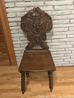Front view of the antique wooden chair showing carved eagle, crossed rifles, antlers, oak leaves, and spindle legs