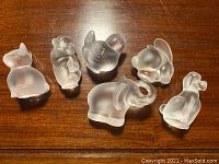 Top view of six crystal animal figurines placed on wooden surface including cat, gorilla, bird, elephant, rabbit and dog shapes.