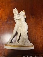 Front view of the porcelain figure showing two nude classical figures embracing on a gold-trimmed base.