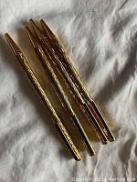 Four gold-tone Jaguar pens with textured barrels lying on white fabric, showing front side and clips.