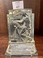Front view of bronze book end showing seated woman and background relief detail.