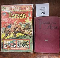 Front covers of both items showing the comic book's colorful DC Tarzan cover and the antique red hardcover Tarzan of the Apes book.