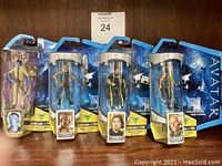 Lot of four Avatar action figures in original packaging, arranged side by side on wooden surface.