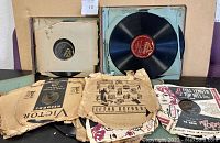 Photo showing a collection of approximately 30 vintage 78 RPM shellac records, many with original Victor Records paper sleeves, placed on a surface.