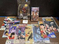 Photo showing all Star Trek collectibles including comic books spread out, the Cadet Chekov action figure in packaging, and the VHS tape of The Cage pilot episode.