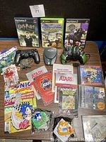 Overview of vintage gaming lot including games, manuals, controllers, comic book, artwork and handheld game device.