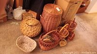 Overview photo of all baskets showing the variety of sizes, shapes, and weaving styles in natural fibers on carpeted floor.