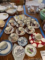 Overview of multiple small porcelain tea cups and saucers, assorted plates, and leaded crystal pieces arranged on a table