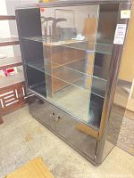 Front view of the black wood display cabinet with glass sliding doors and lower wood cabinet doors, sitting on a concrete floor.