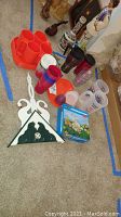 Photo showing various plastic cups in orange, white, red, and maroon colors arranged on floor plus Easter mold box and swan key rack
