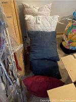 Photo showing 2 white quilted feather pillows and 4 throw pillows in red, dark blue, and grayish blue colors stacked against a wall.