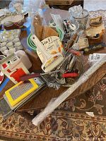 Wide view of assorted kitchen items including jadeite bowls, wooden butter molds, graters, cutlery, metal nut picks, and various utensils on a table.
