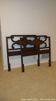 Two images showing each wooden twin headboard upright against a wall with carved symmetrical scrollwork and scalloped pattern designs.
