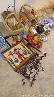Photo of nested baskets with pottery houses, nesting dolls, small plates, and a wool tapestry laid out on carpet.