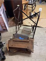 Photo showing disassembled sewing machine table components and metal frame with treadle pedal base.