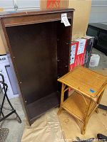 Wooden bookcase standing upright next to the bamboo side table, showing open interior and shelf peg holes