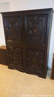 Front view of closed dark wood cabinet with decorative carved panel doors