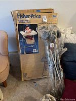 Full view of boxed Fisher-Price high chair and folded stroller leaning against the box.