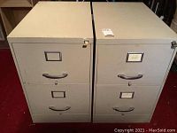 Two off white/light gray metal file cabinets with two drawers each, locks and keys included, showing signs of wear