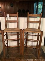 Front view of two wooden bar height ladder back chairs with woven seats, showing the ladder style backs and woven seats.